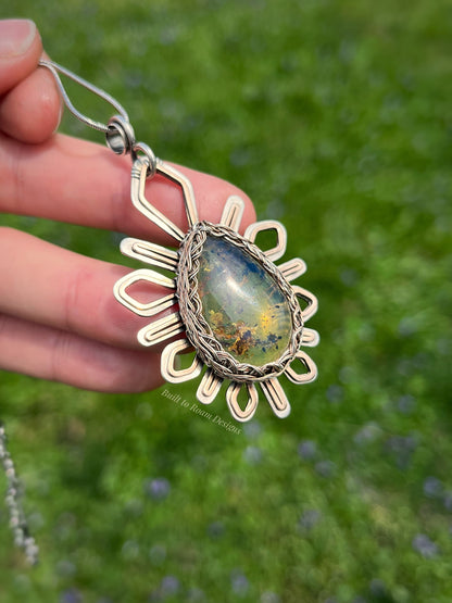 Side view of hand holding a silver and bronze star-burst pendant with a golden amber gemstone - Liora