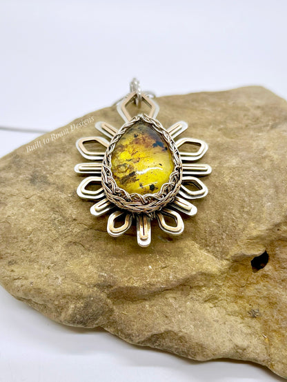 Silver and bronze star-burst pendant with a golden amber gemstone on a rock - Liora