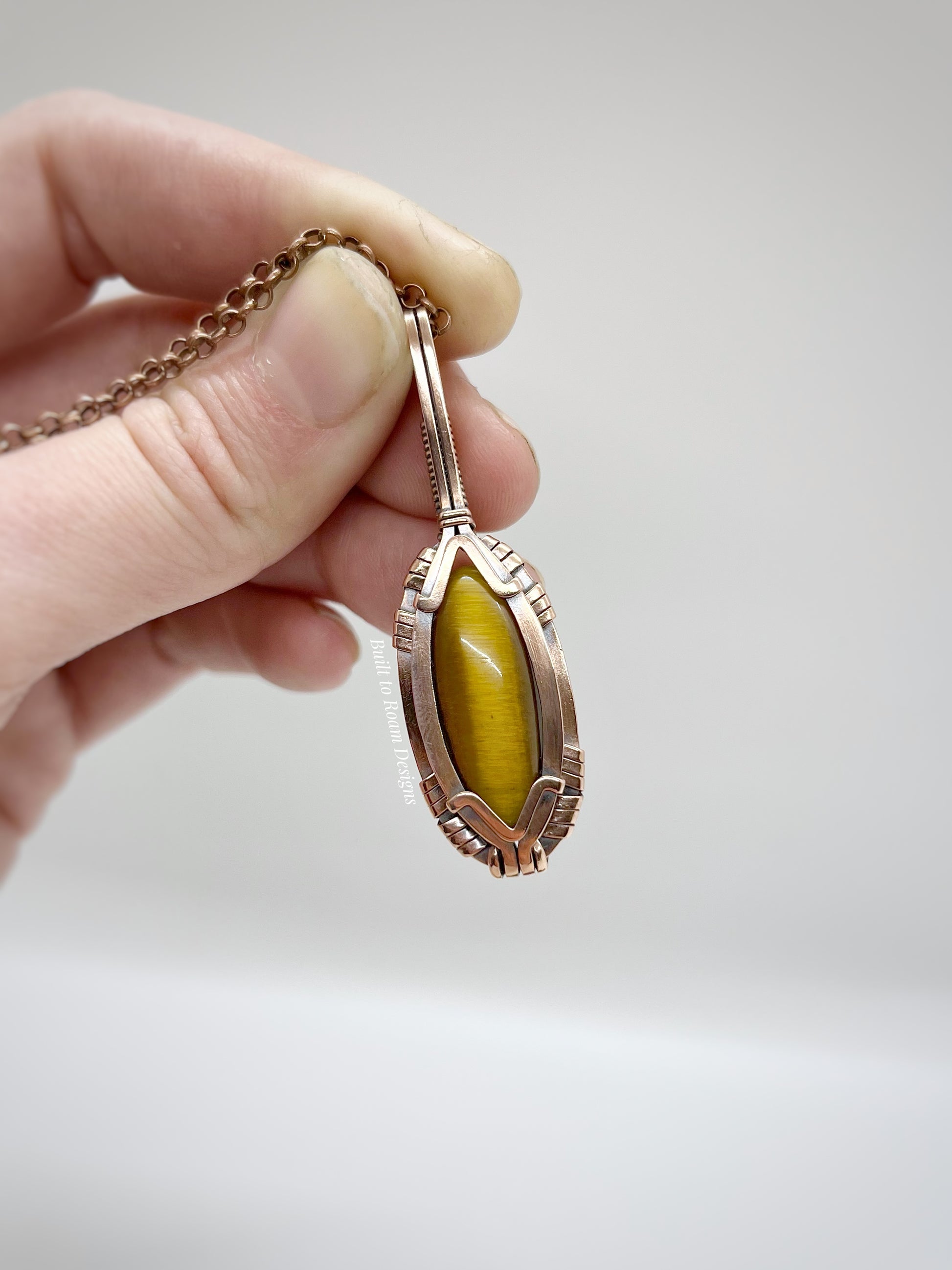 Hand holding a copper pendant with tigers eye against a light background