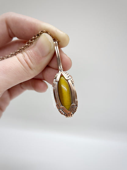 Hand holding a copper pendant with tigers eye against a light background