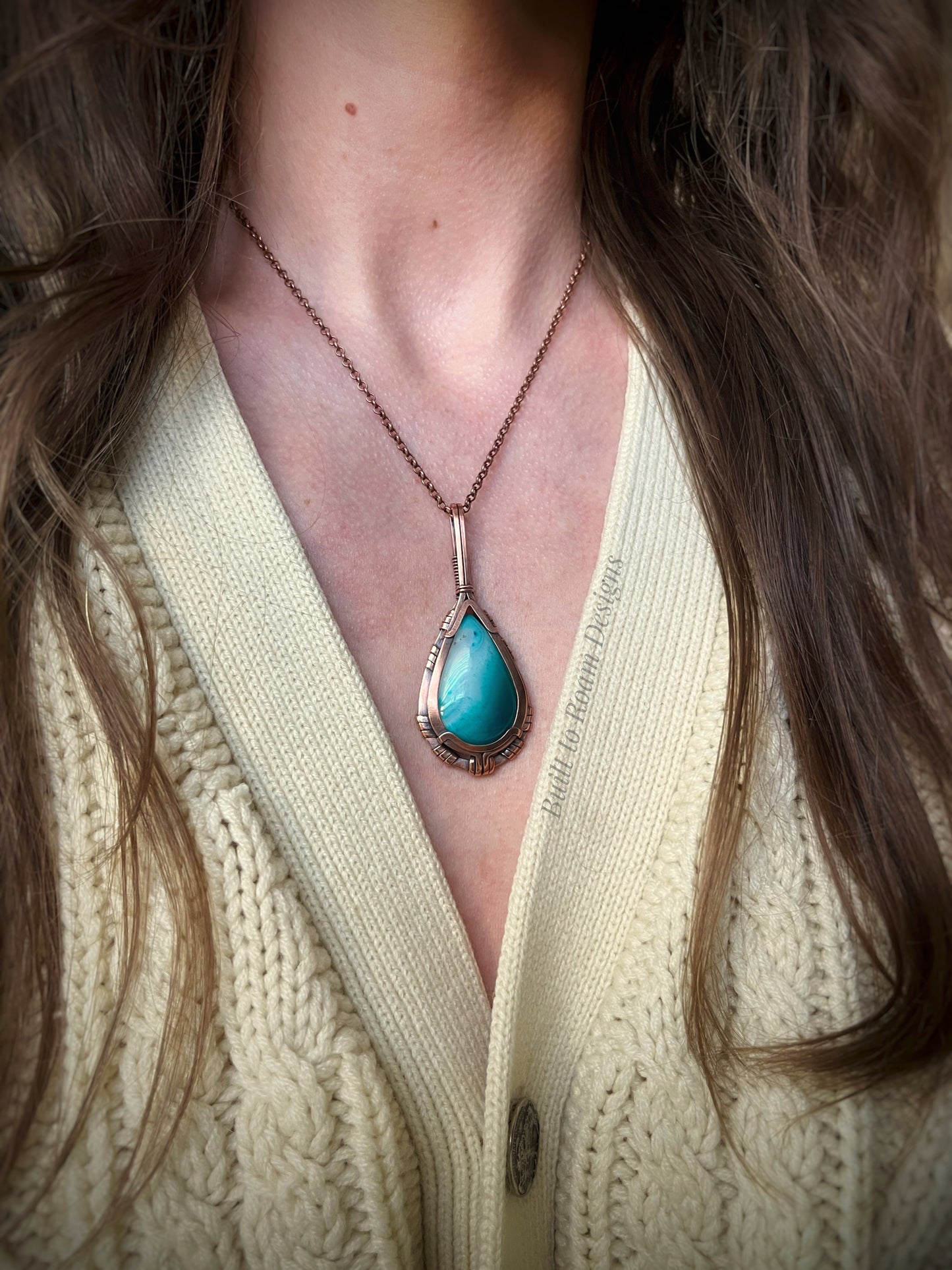 Turquoise color enhanced banded agate pendant necklace on a person wearing a light-colored sweater