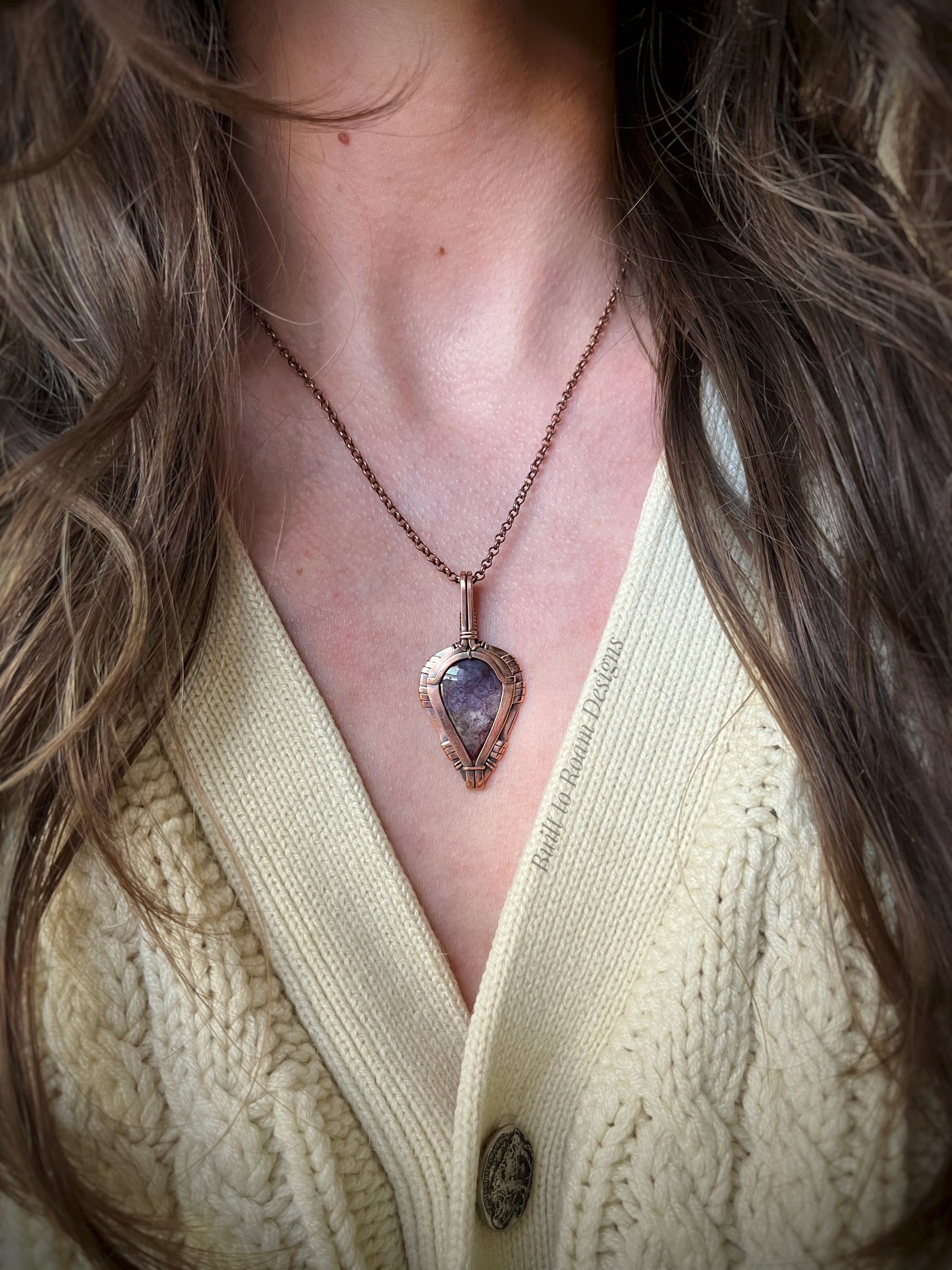 copper necklace with a purple moss agate pendant worn by a person in a cream sweater