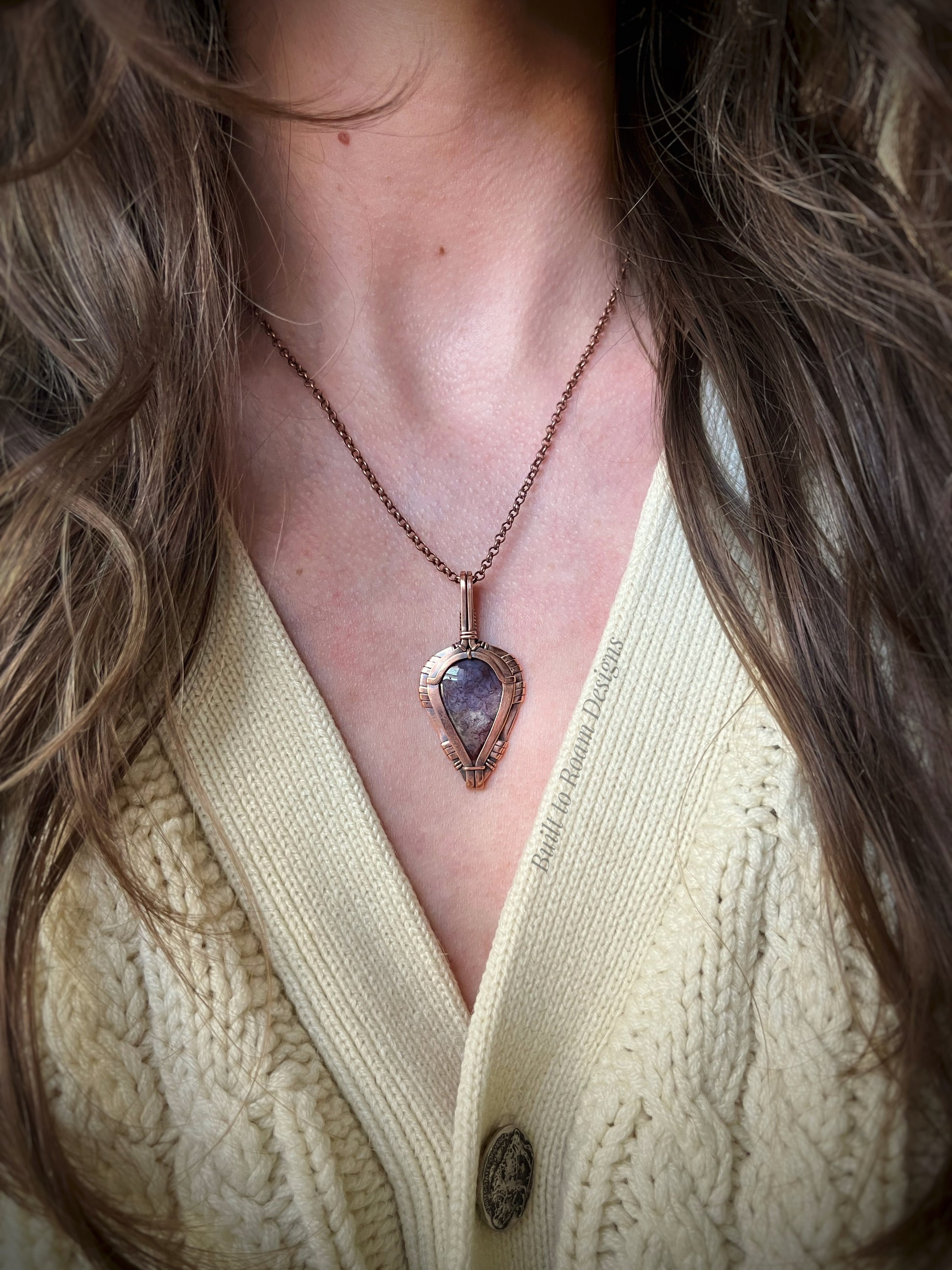 copper necklace with a purple moss agate pendant worn by a person in a cream sweater
