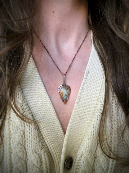 Necklace with a peruvian opal in copper pendant worn by a person in a light-colored sweater.